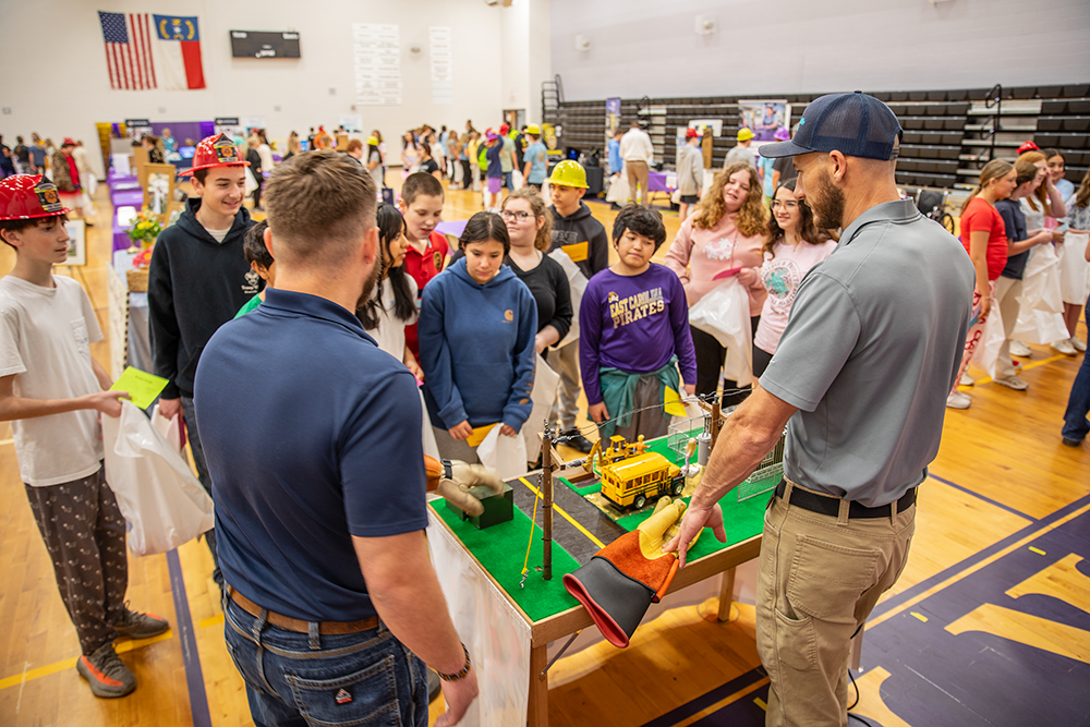 Group of children watching an electricity demonstration at a school career fair.